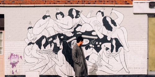 Man in black coat stood in front of mural Man in black coat stood in front of mural