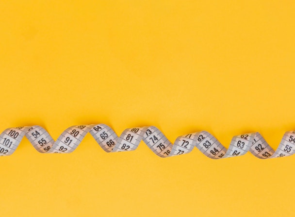 A twisted tape measure against a yellow background A twisted tape measure against a yellow background