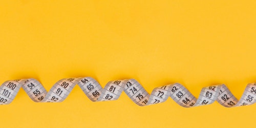 A twisted tape measure against a yellow background A twisted tape measure against a yellow background