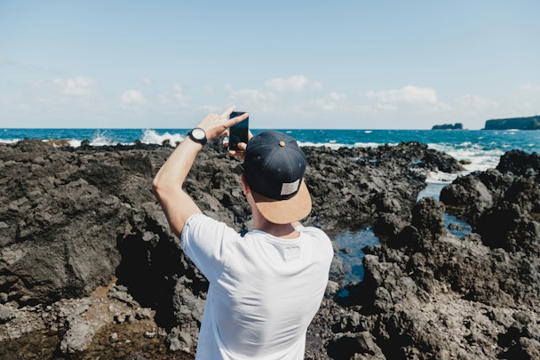 A man uses his phone to take a photo of the sea and a rocky shoreline A man uses his phone to take a photo of the sea and a rocky shoreline