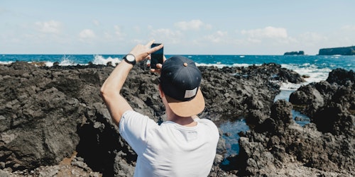 A man uses his phone to take a photo of the sea and a rocky shoreline A man uses his phone to take a photo of the sea and a rocky shoreline