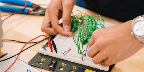 A person's hands adjust wires on a rudimentary computer A person's hands adjust wires on a rudimentary computer
