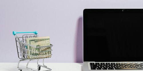 A shopping trolley containing bank notes next to a laptop, representing omnichannel customer service in the retail sector A shopping trolley containing bank notes next to a laptop, representing omnichannel customer service in the retail sector