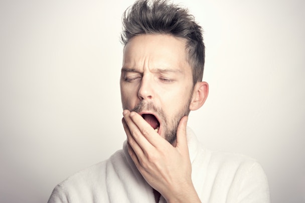A man in a light-colored shirt raises his hand to his mouth as he yawns A man in a light-colored shirt raises his hand to his mouth as he yawns