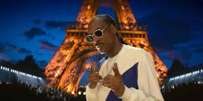 Snoop Dogg holdign a microphone and giving the peace sign with his fingers