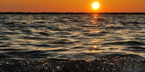 The sun low over the sea with waves breaking on the beach The sun low over the sea with waves breaking on the beach